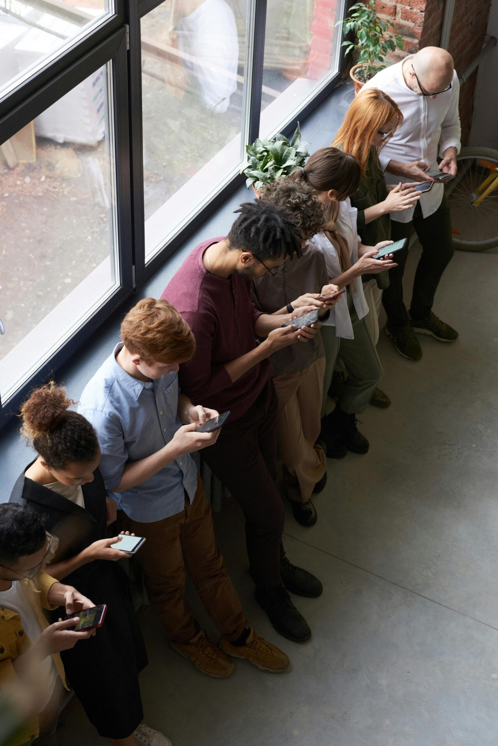 pexels-photo-3184435-3184435 - YIFAN BUSINESS SERVICES LTD A group of diverse office workers standing by a window using smartphones, capturing modern workplace connectivity.